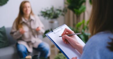 Unrecognizable professional female psychologist writing on clipboard while sitting against client on blurred background during psychotherapy session in light office